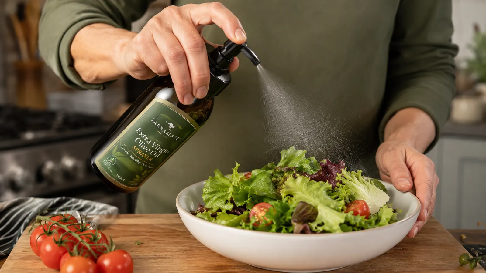 Hand misting olive oil from a glass sprayer over a salad in a white bowl