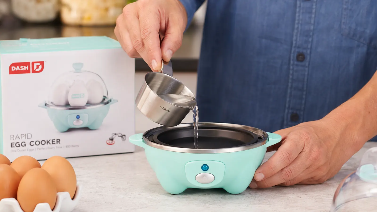 Close-up of the Dash egg cooker measuring cup filled to the hard-boiled line, held over the heating plate