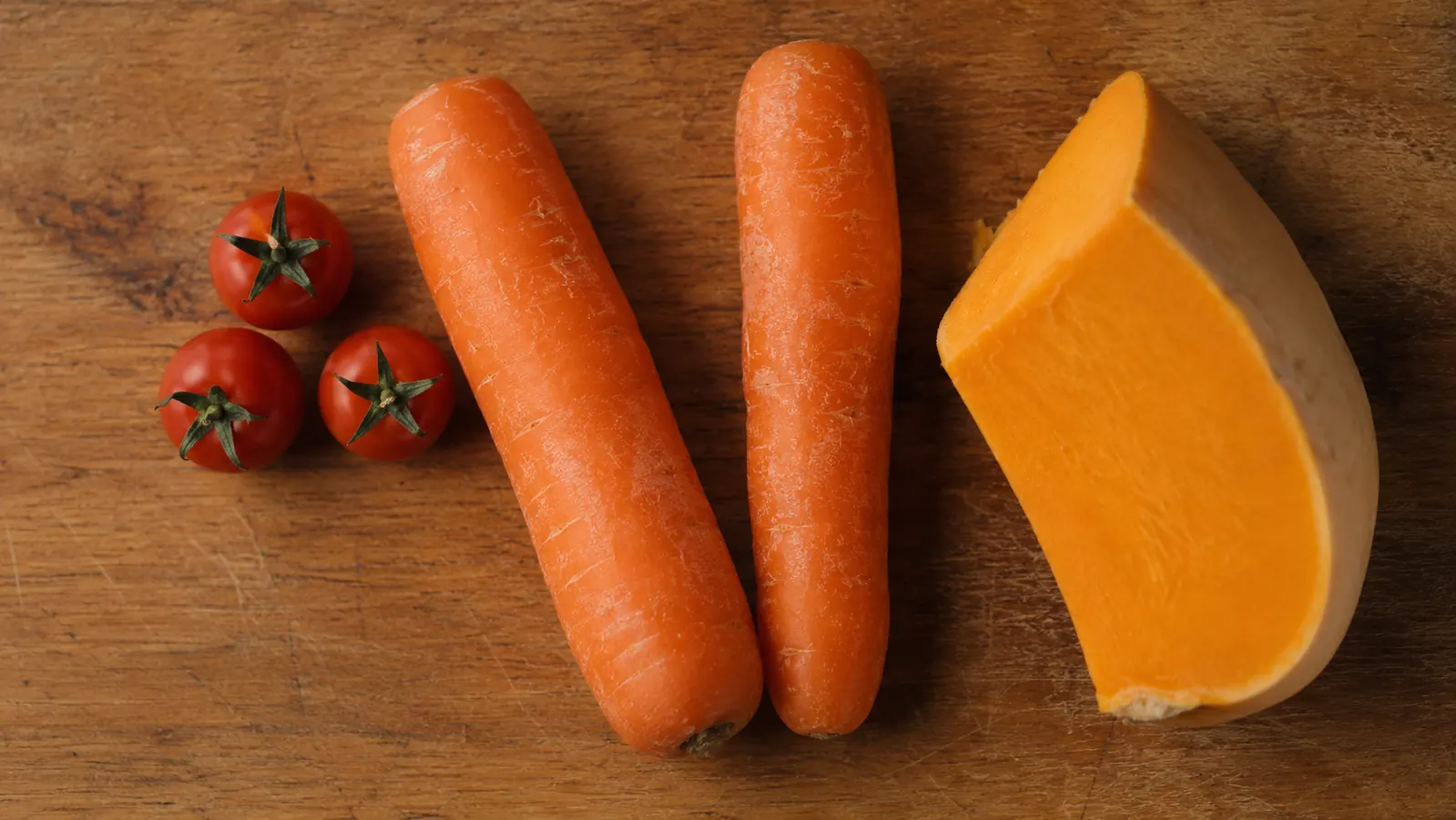 Collection of vegetables the Fullstar struggles with: whole cherry tomatoes, thick raw carrots, and a butternut squash on a cutting board
