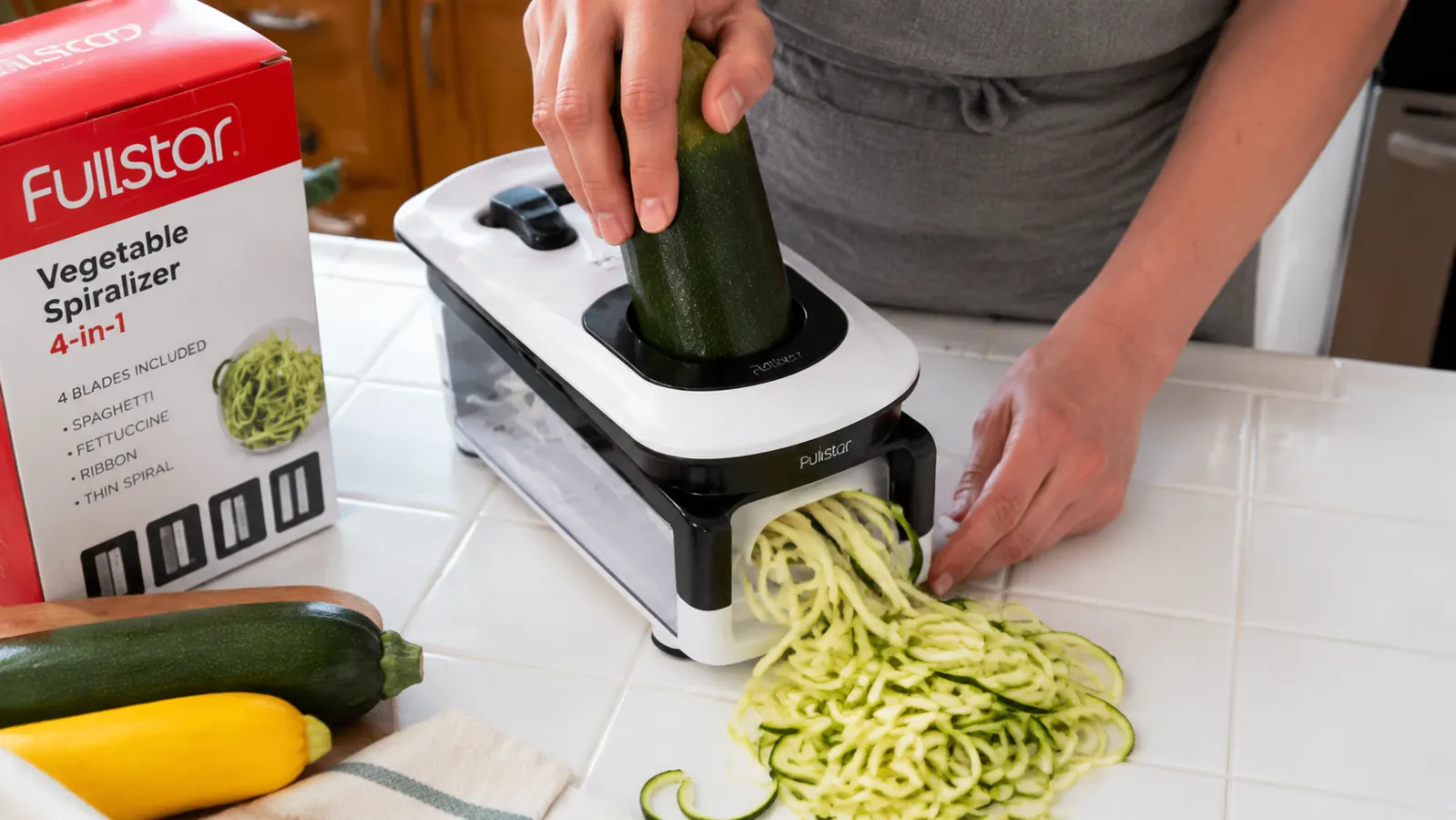 Hand pressing zucchini through the Fullstar spiralizer suction base locked onto a white kitchen counter