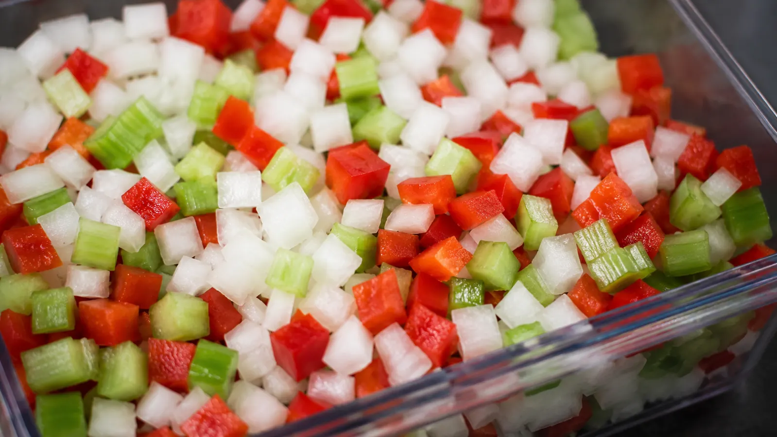 Close-up of uniformly diced onion, red pepper, and celery pieces in a clear container