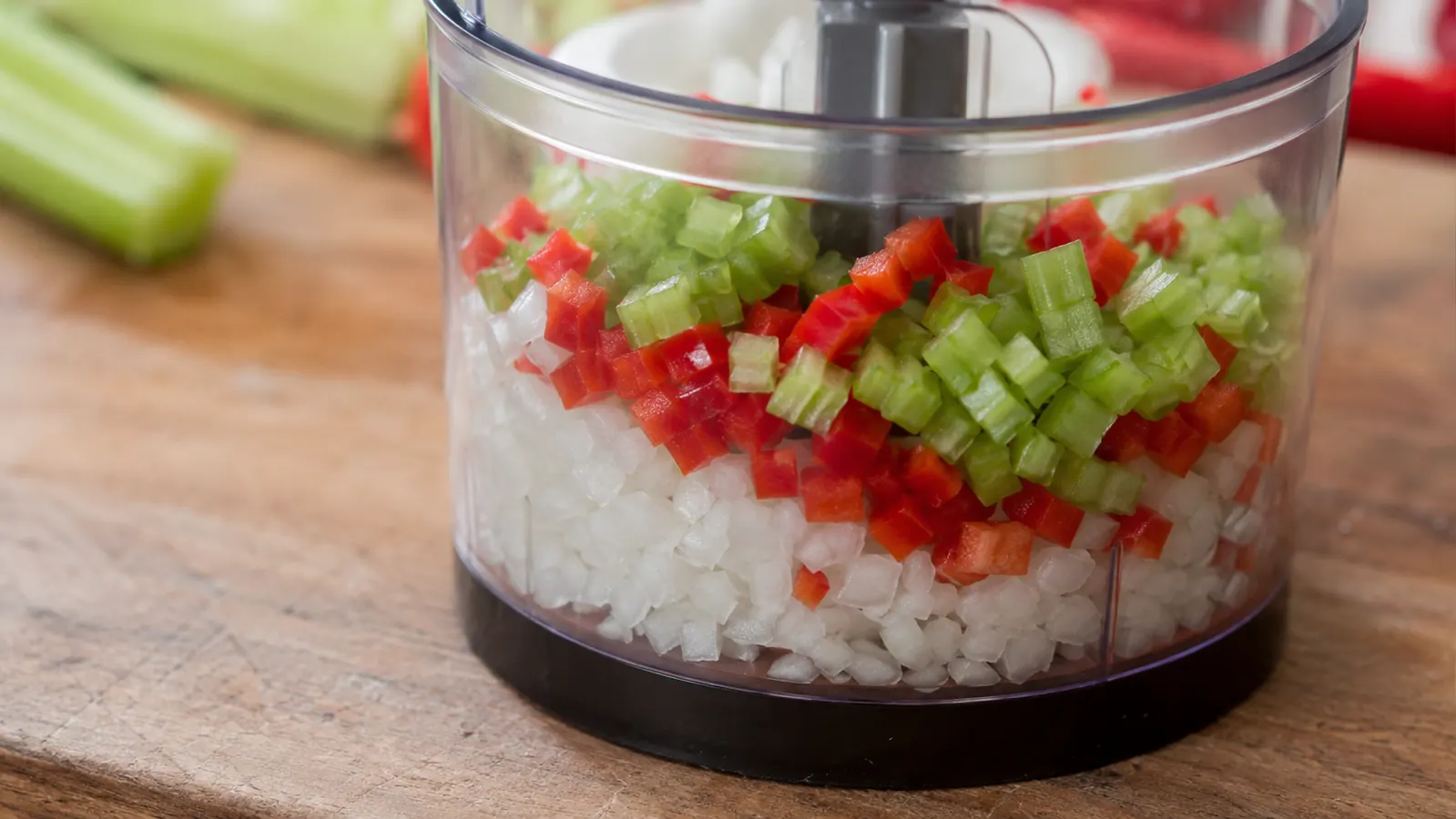 Diced onion, red pepper, and celery in the clear collection container of a vegetable chopper